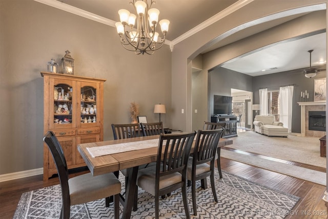 dining room with arched walkways, wood finished floors, crown molding, and a tile fireplace