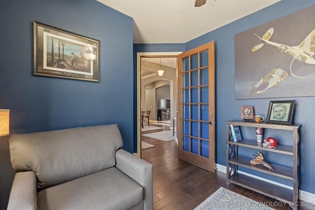 living area featuring a ceiling fan, wood finished floors, arched walkways, and baseboards