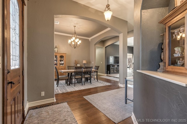 dining area featuring dark wood-style floors, baseboards, arched walkways, ornamental molding, and a textured wall