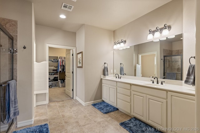 bathroom with visible vents, a walk in closet, a sink, a shower stall, and double vanity