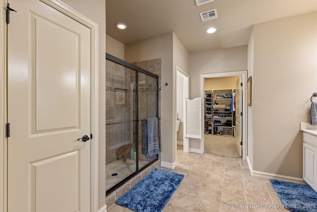 bathroom featuring vanity, baseboards, visible vents, a shower stall, and a spacious closet