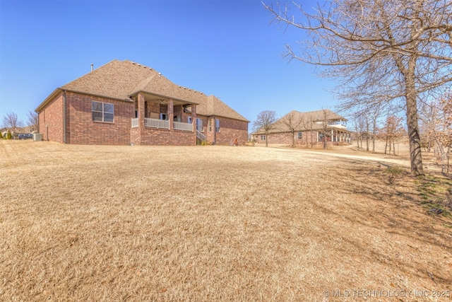 back of property featuring a yard, brick siding, a porch, and a shingled roof