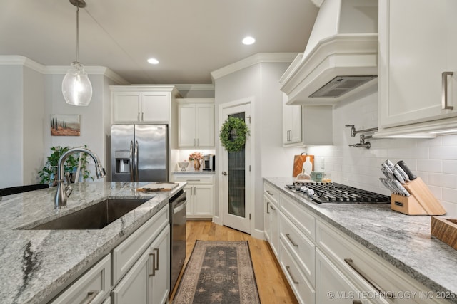 kitchen featuring premium range hood, appliances with stainless steel finishes, hanging light fixtures, white cabinetry, and a sink