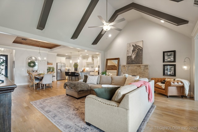 living room featuring visible vents, high vaulted ceiling, light wood-style flooring, ceiling fan with notable chandelier, and a tray ceiling