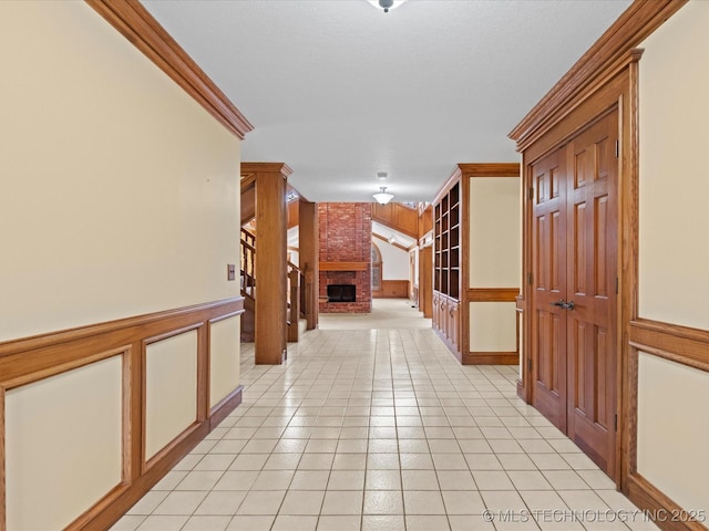 hallway featuring light tile patterned flooring, wainscoting, and ornamental molding