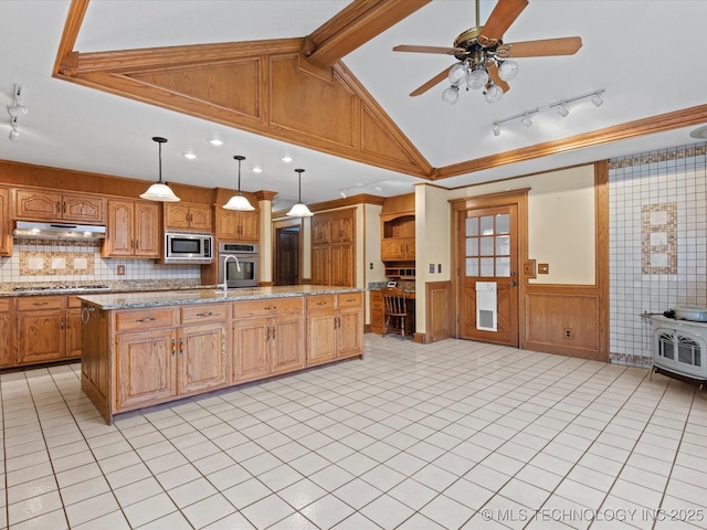 kitchen with a wainscoted wall, under cabinet range hood, lofted ceiling with beams, appliances with stainless steel finishes, and a wood stove