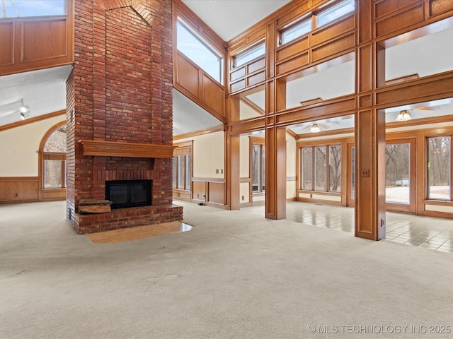 unfurnished living room featuring a wainscoted wall, a high ceiling, a fireplace, crown molding, and carpet flooring