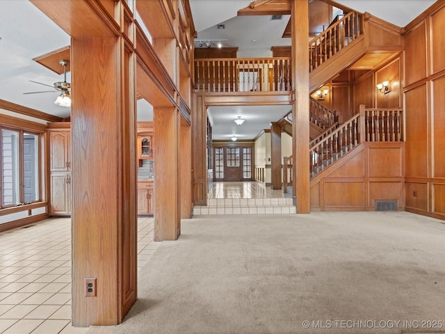 unfurnished living room with wooden walls, stairs, carpet floors, a towering ceiling, and tile patterned floors