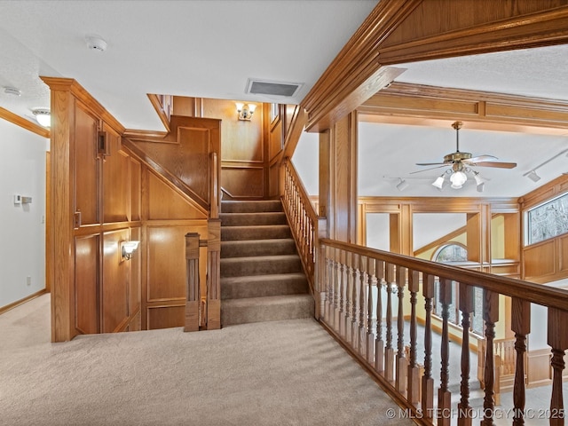 staircase featuring wooden walls, visible vents, crown molding, carpet, and a ceiling fan