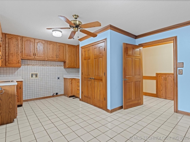 kitchen with brown cabinets, light countertops, a ceiling fan, and ornamental molding