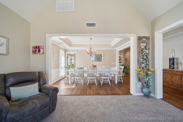 carpeted dining space with a chandelier, visible vents, a tray ceiling, and lofted ceiling