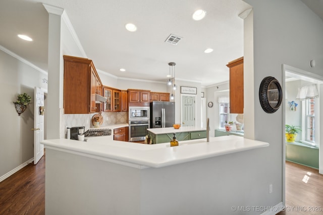 kitchen featuring brown cabinetry, light countertops, appliances with stainless steel finishes, under cabinet range hood, and backsplash