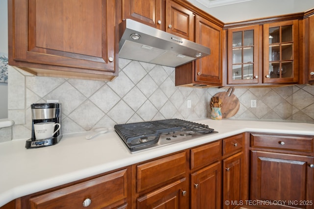 kitchen with range hood, decorative backsplash, light countertops, stainless steel gas stovetop, and glass insert cabinets