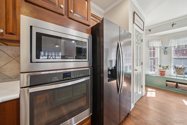 kitchen featuring brown cabinets, stainless steel appliances, light wood-type flooring, and ornamental molding