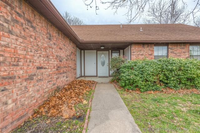 doorway to property featuring brick siding and a shingled roof