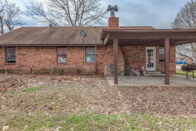 rear view of property featuring a patio, brick siding, roof with shingles, and a chimney