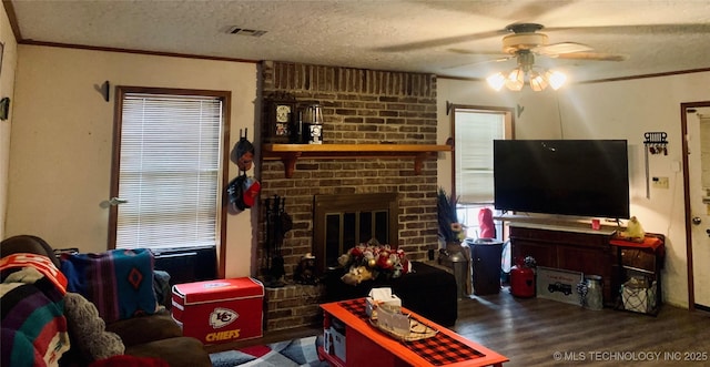 living area featuring wood finished floors, visible vents, ornamental molding, a textured ceiling, and a brick fireplace