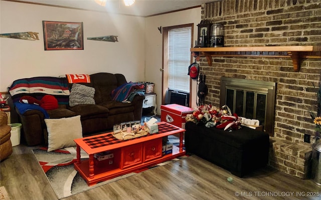 living room with crown molding, a brick fireplace, and wood finished floors