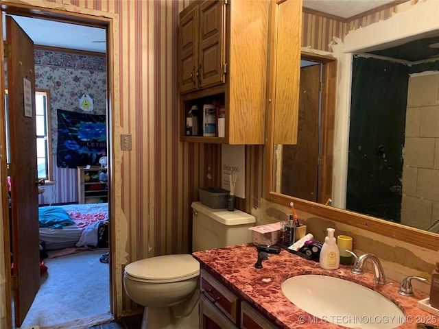 bathroom featuring toilet, vanity, and wallpapered walls