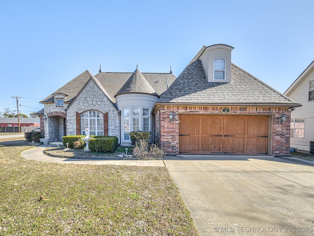 french country inspired facade featuring a front lawn, brick siding, an attached garage, and driveway