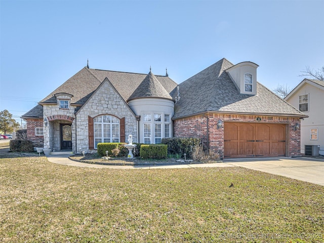 french country style house with a front yard, driveway, a garage, central air condition unit, and brick siding