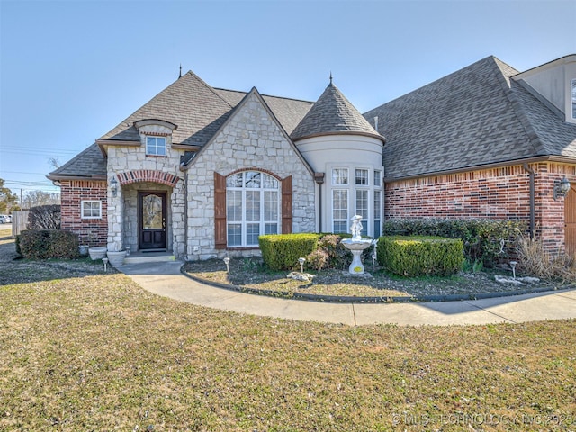 french country inspired facade with a front yard, brick siding, and roof with shingles