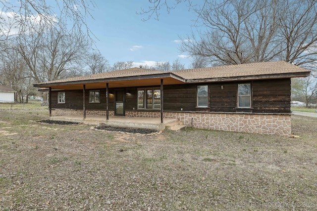 rear view of house with stone siding, a shingled roof, and a patio