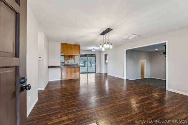 unfurnished living room featuring visible vents, baseboards, and dark wood-style floors