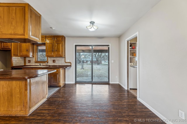 kitchen featuring dark countertops, baseboards, decorative backsplash, dark wood-style floors, and washer / clothes dryer