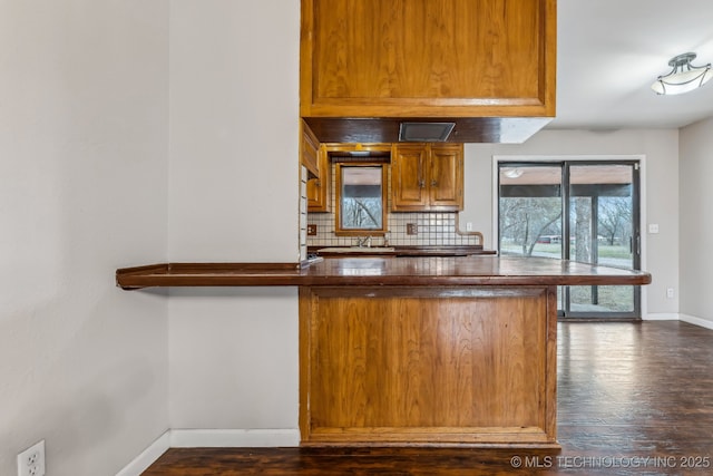 kitchen featuring backsplash, dark countertops, dark wood finished floors, a peninsula, and baseboards