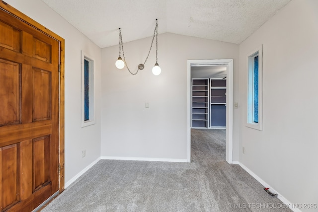 carpeted empty room featuring a textured ceiling, baseboards, and vaulted ceiling