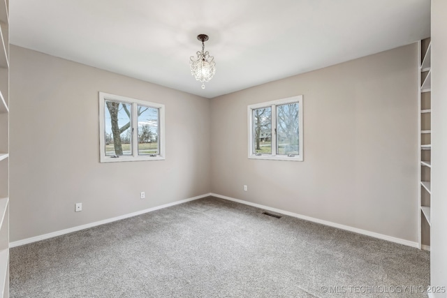 carpeted spare room with a notable chandelier, baseboards, and visible vents