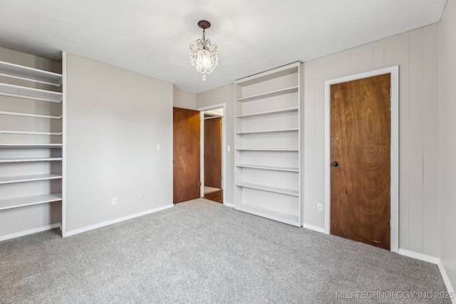 unfurnished bedroom with baseboards, a notable chandelier, and carpet flooring