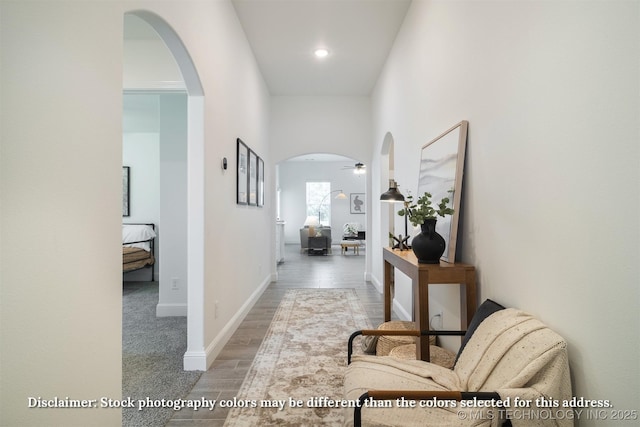 hallway with wood finished floors, arched walkways, and baseboards