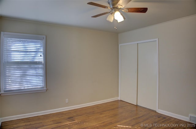 unfurnished bedroom featuring a ceiling fan, wood finished floors, a closet, crown molding, and baseboards