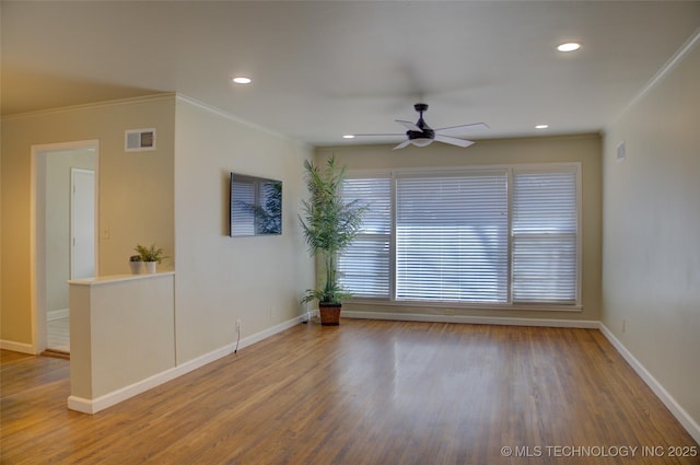 empty room featuring visible vents, wood finished floors, baseboards, and ornamental molding