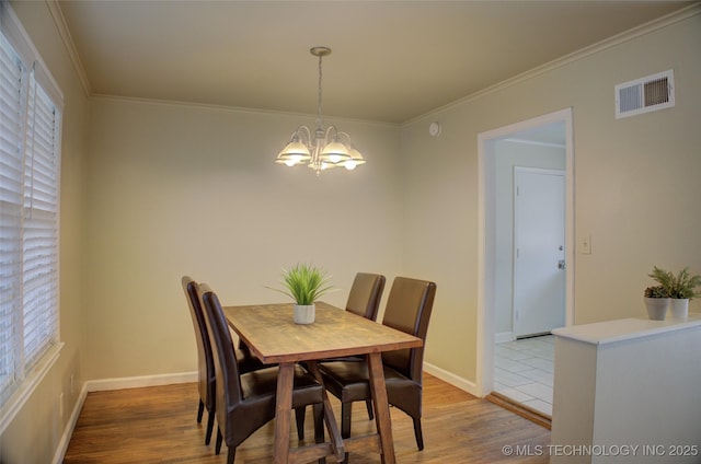 dining space with visible vents, baseboards, ornamental molding, light wood-style floors, and an inviting chandelier