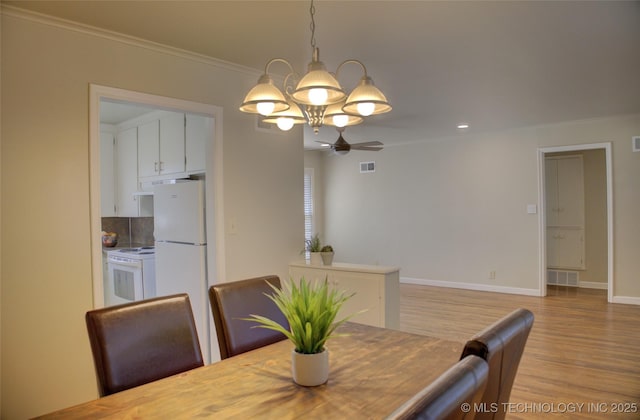 dining space featuring light wood-type flooring, visible vents, an inviting chandelier, crown molding, and baseboards