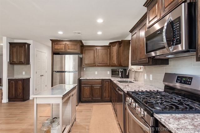 kitchen with visible vents, a sink, appliances with stainless steel finishes, light stone countertops, and backsplash