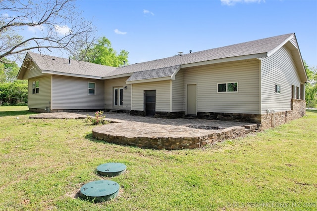 back of house featuring roof with shingles, a patio, and a lawn