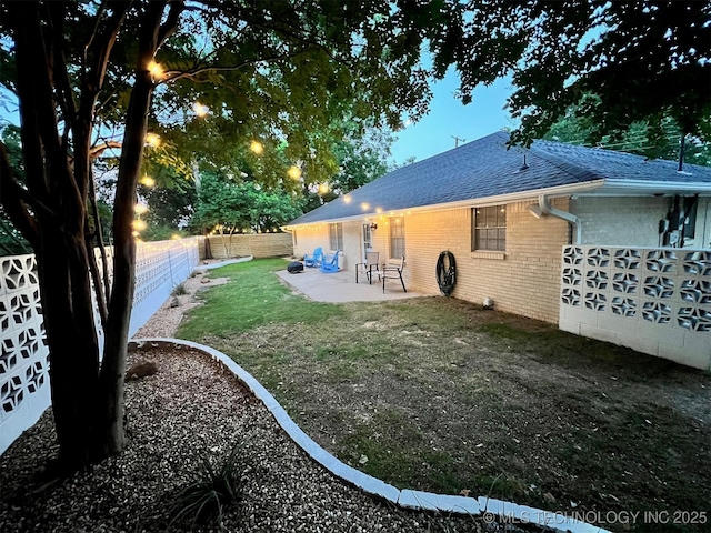 rear view of house with brick siding, roof with shingles, a yard, a fenced backyard, and a patio area