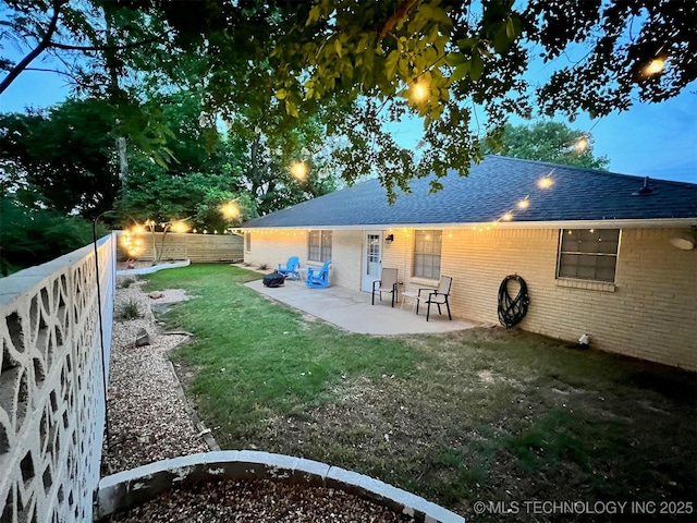 back of house featuring brick siding, a shingled roof, a lawn, a fenced backyard, and a patio