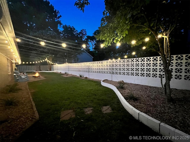 yard at night with an outdoor fire pit and a fenced backyard