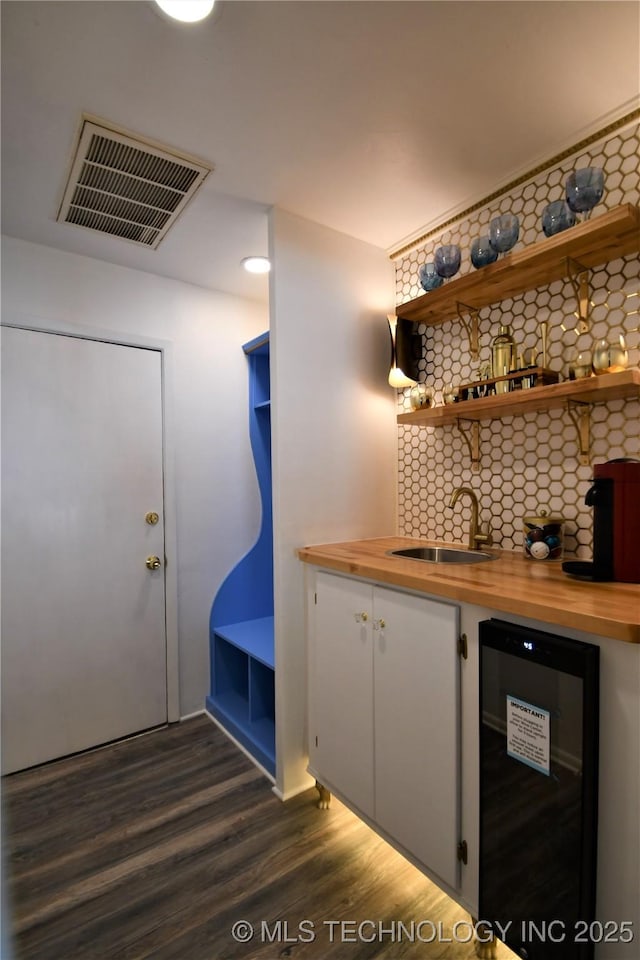 bar with beverage cooler, visible vents, dark wood finished floors, and a sink