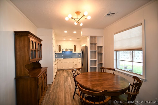 dining area with visible vents, dark wood-type flooring, crown molding, and a notable chandelier