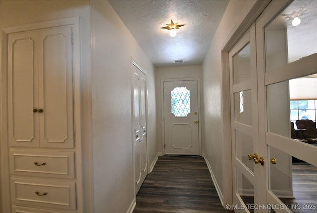 doorway to outside with visible vents, a textured ceiling, baseboards, and dark wood-style flooring