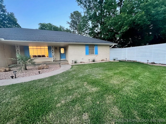 view of front of house with a front lawn, fence, brick siding, and roof with shingles