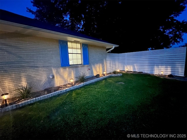 property exterior at twilight featuring brick siding, a lawn, and fence