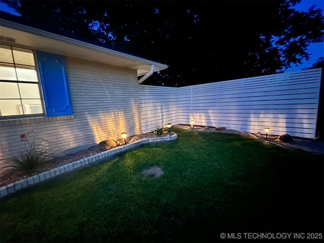 yard at night featuring a fenced backyard