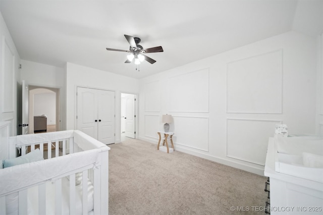 bedroom featuring a closet, a decorative wall, light colored carpet, and ceiling fan